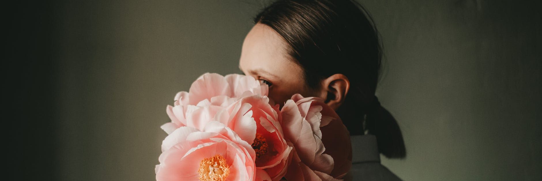 young female covering face with bouquet of flowers in dark room